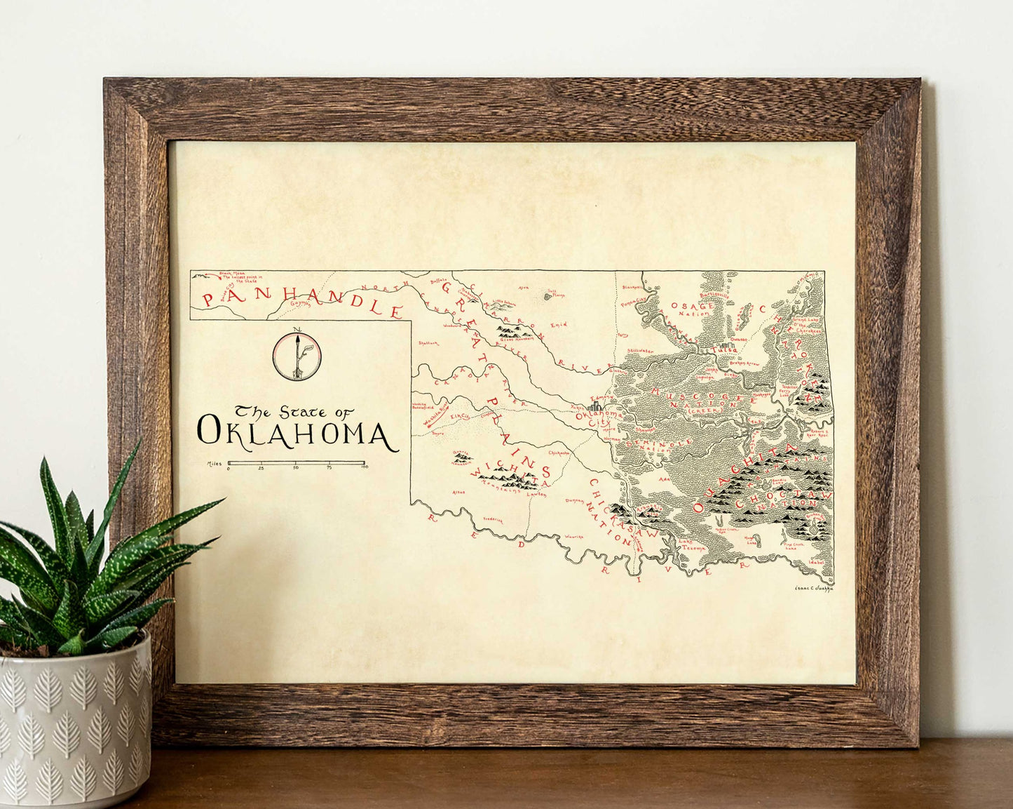 The Oklahoma NEW Updated Version framed art print by Lord of Maps features a vintage hand-drawn map labeled "The State of Oklahoma," with intricate details and red markings, displayed beside a small green succulent on a white surface.