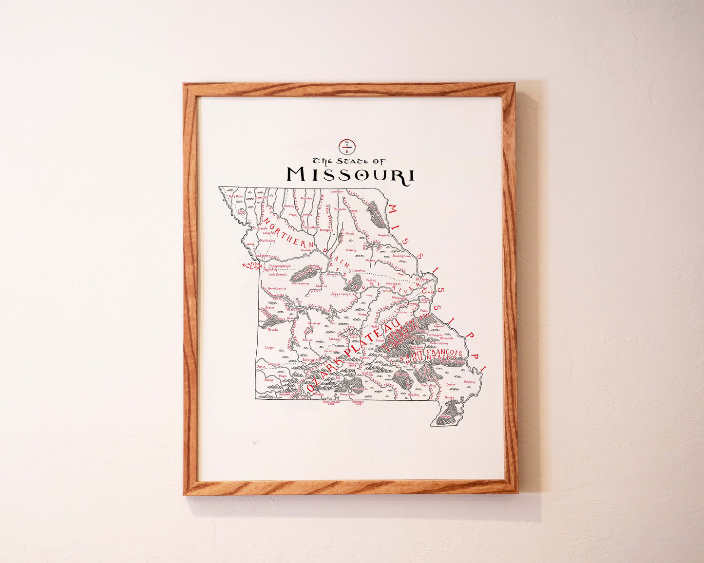 A framed map of Missouri hangs on a white wall, showing state borders, major rivers, and cities, with The State of Missouri written at the top in bold letters.