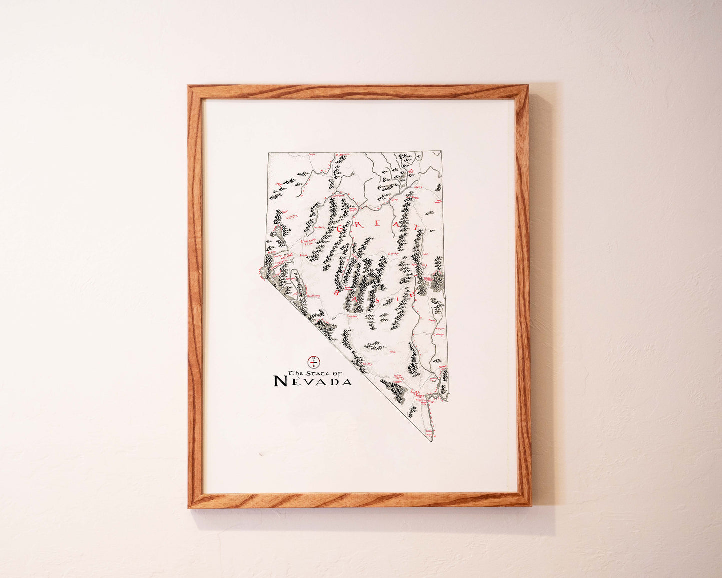 A framed map of the state of Nevada hangs on a light-colored wall. The map features outlined borders, marked locations, and mountain ranges, with “The State of Nevada” written at the bottom.
