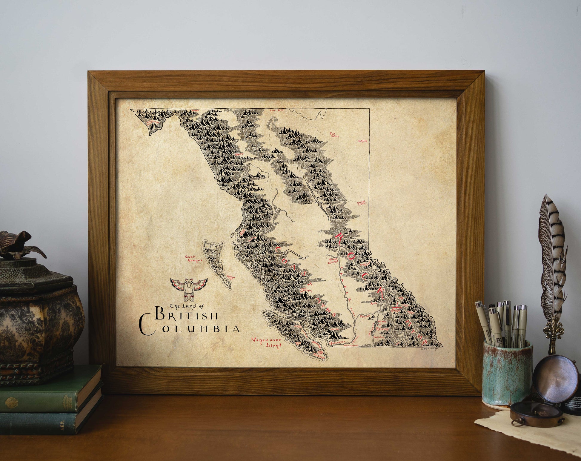 The British Columbia Map by Lord of Maps is a framed, hand-drawn print displayed on a shelf among books and art supplies—a charming piece of vintage-style wall art.