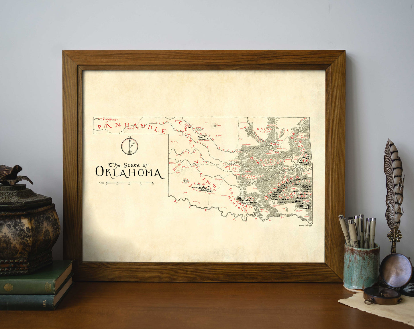 The Oklahoma NEW Updated Version framed art print by Lord of Maps features a vintage-style, hand-drawn map labeled "The State of Oklahoma," displayed on a wooden desk with books, a decorative jar, an ink bottle, and a quill pen.