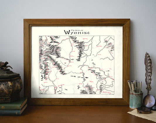 The Wyoming Map by Lord of Maps, a vintage-style framed print with handwritten labels and rich illustrations, is displayed on a shelf beside books, a decorative box, and a quill in an inkwell.